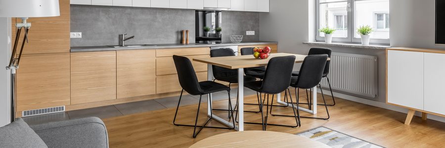 Esstisch mit heller Holzplatte auf weissem Metallgestell und vier schwarzen Stuehlen in einer offenen Wohnkueche